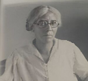 Portrait of Aurelia Godfrey Mitchell (1859 to 1940), a Black Creole woman from Lafayette Parish, Louisiana, who settled in Liberty County, Texas. She is shown seated, wearing a light-colored blouse, with silver hair parted in the center and round wire-frame glasses. Photograph hosted on Find a Grave Memorial ID 90549631.